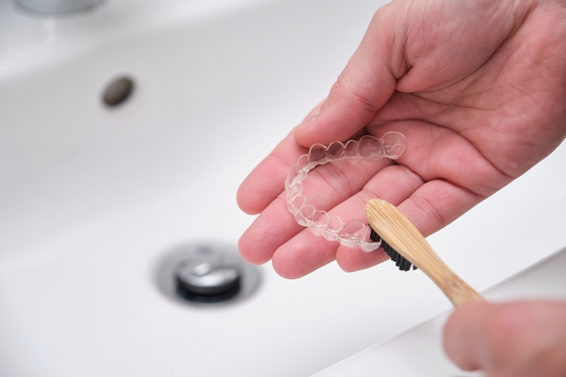 Cleaning tooth aligners. Washing and removing organic residues with a bamboo toothbrush from orthodontic invisible braces.